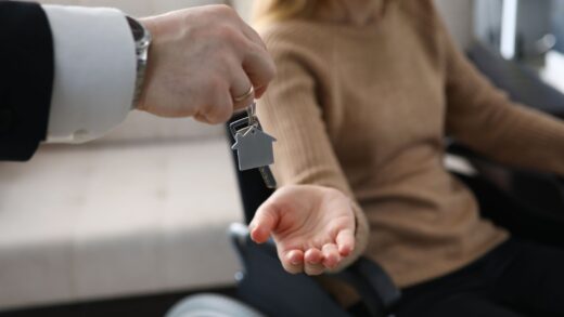 Zbliżenie na biznesmena wręczającego klucze od nowego domu niepełnosprawnej kobiecie. Kobieta siedząca na wózku inwalidzkim. Dzień przeprowadzki do mieszkania. Niepełnosprawni i koncepcja nieruchomości